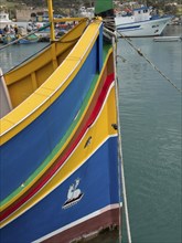 Detailed view of the bow of a colourful boat with other boats in the background on calm water, many