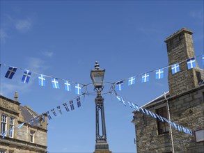 Street scene with blue and white flags hanging from a lamppost between old buildings, calm sea with