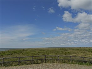 Extensive view of the sea and a green meadow under a partly cloudy sky, dune and beach by the sea