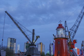 Red lighthouse in the harbour with cranes and skyscrapers in the background at dusk, small harbour