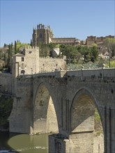 Stone bridge with arches over a river, in the background a church and cityscape, sunny weather,