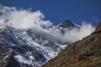Snow covered peaks with clouds floating around the mountains under a clear blue sky, snow on high