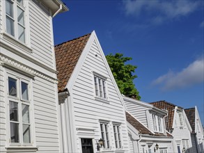 A row of white wooden houses with windows and red roof tiles under a blue sky in the sunshine,
