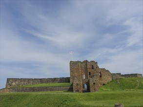 Castle ruins with walls in the background, surrounded by green grass with flag in the wind under a
