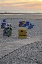Various beach chairs and a wooden path on a sandy beach at sunset, many colourful beach chairs on a