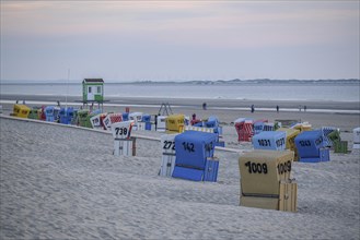 Beach with colourful beach chairs at dusk, by the sea in a dune landscape. People walking along the