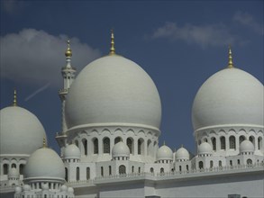 Detailed view of the white domes of a mosque with golden spires against a blue sky, large mosque