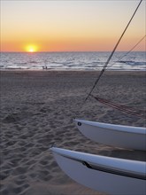 Boats on the beach at sunset, the sea glistens under the orange sky, a calm and relaxed atmosphere,
