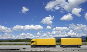 A yellow lorry drives on the A3 motorway under a blue sky with white clouds, motion blur, Bavarian