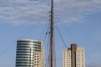 Sail mast between two modern buildings in front of a blue sky, skyline of a modern city on a river