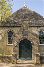 Historic building with curved entrance portal and green door, surrounded by trees and blue sky, old