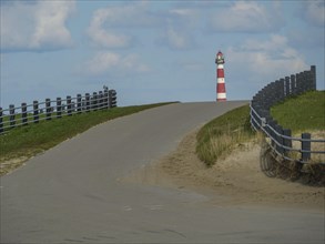 Road leads slightly uphill to a lighthouse, flanked by fences, with cloudy sky, red and white