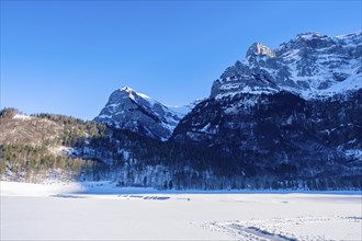 Snow-covered mountains and a frozen lake under a clear blue sky in a winter landscape, Kloental,