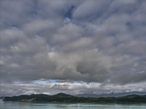 Wide cloud cover over a calm body of water, with gentle mountains on the horizon, greenish