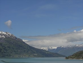 Calm waters with snow-capped mountains under a clear blue sky, greenish shimmering water in a fjord