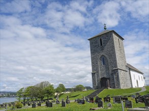 Church with cemetery under a cloudy sky on a green meadow, old stone church and many gravestones by
