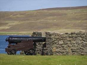 Old cannon in front of a stone wall with sea view and hills in the background, old cannon on a