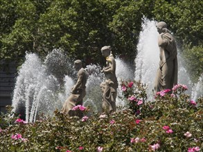 Three statues in a fountain surrounded by blooming flowers and bubbling water fountains, fountain