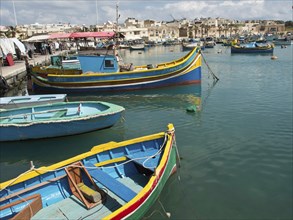 Harbour view with several colourful boats on calm water and a town in the background, many