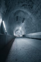 A long, barren tunnel with minimalist lighting and concrete walls that radiates a cold and harsh