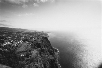 Black and white view of a coastal landscape with a steep cliff and the sea in the background.