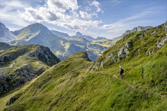Mountaineer on a hiking trail on a grassy mountain ridge, idyllic mountain landscape with green
