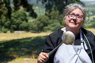 Woman cook in white apron with a spatula in her hand smiling in the field