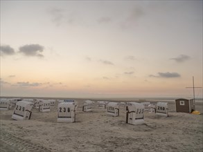Beach chairs standing in the sand under a pastel-coloured sky at sunset, the atmosphere is peaceful