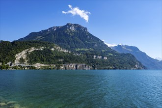 Clear water of a lake in front of an impressive mountain landscape under a blue sky with scattered