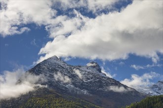 Snow covered mountain peak under a blue sky with scattered clouds, snow on high mountains in the