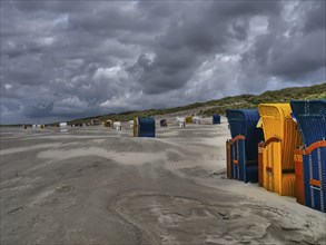 Colourful beach chairs on a wide, deserted beach under a dramatic sky, colourful beach chairs on