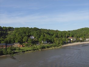 Expansive river view with green hills and scattered buildings on the shore, green bank on a river