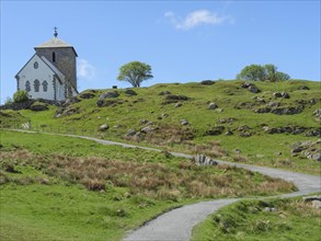 Church with hiking trail on hilly landscape, blue sky with clouds and trees, old stone church and