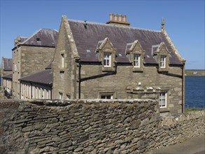 Stone building with skylights behind a stone wall, on a clear day by the sea, old stone house by