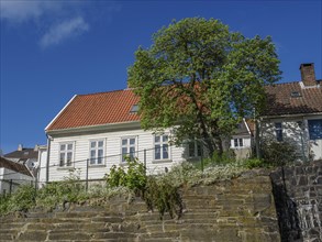 White house with red tiled roof behind a stone wall under blue sky, white wooden houses with red