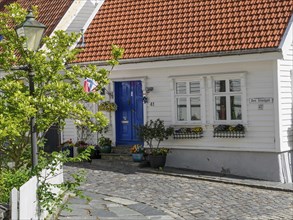White houses with tiled roofs, blue sky, lantern, plant pots, cobblestone street, white wooden