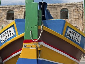 Colourful bow of a boat with the inscription ROCKY II VALLETTA, in front of an old building with