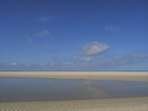 Shallow water and a wide beach under a clear blue sky, wide sky on the lonely North Sea beach with