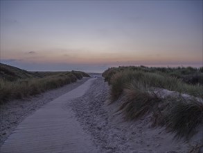 Twilight scene with wooden path through dunes, leading to the sea at sunset, setting sun on a beach