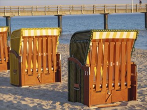 Beach chairs in the sunlight on the sandy beach, with sea and pier in the background, beach chairs