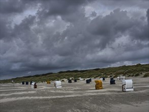 Abandoned beach chairs standing on the beach under a dark, stormy sky, colourful beach chairs on