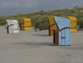 Various beach chairs in bright colours on the sandy beach next to the dunes, sky with clouds,