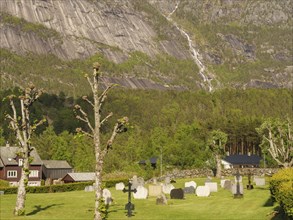 Cemetery with various graves and trees under a steep mountain landscape, gravestones with a small