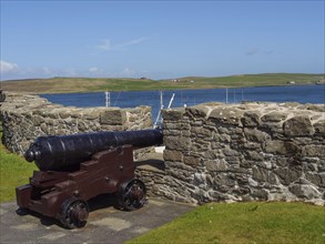 Old cannon standing in front of a stone wall with sea view and green hills under blue sky, old