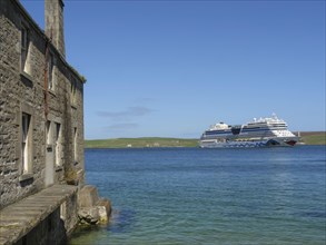 Old stone building with a large cruise ship in clear blue water and bright blue sky, old stone