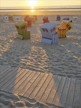 Beach chairs at sunset, projecting shadows on the sand next to a wooden walkway by the sea, sunset