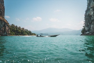 Boat glides on clear water near majestic rock formations. Khao Sok National Park, Thailand, Asia