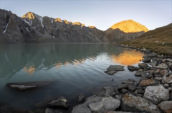 Mountains reflected in the lake, sunrise at the turquoise Ala Kul mountain lake, shining yellow