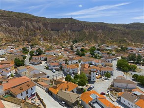 Panoramic view of a village with orange roofs, streets and green trees surrounded by mountains,
