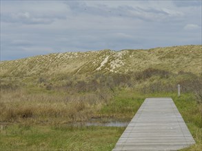 A wooden walkway ends in a sandy dune landscape under a cloudy sky, wooden path through the dune,